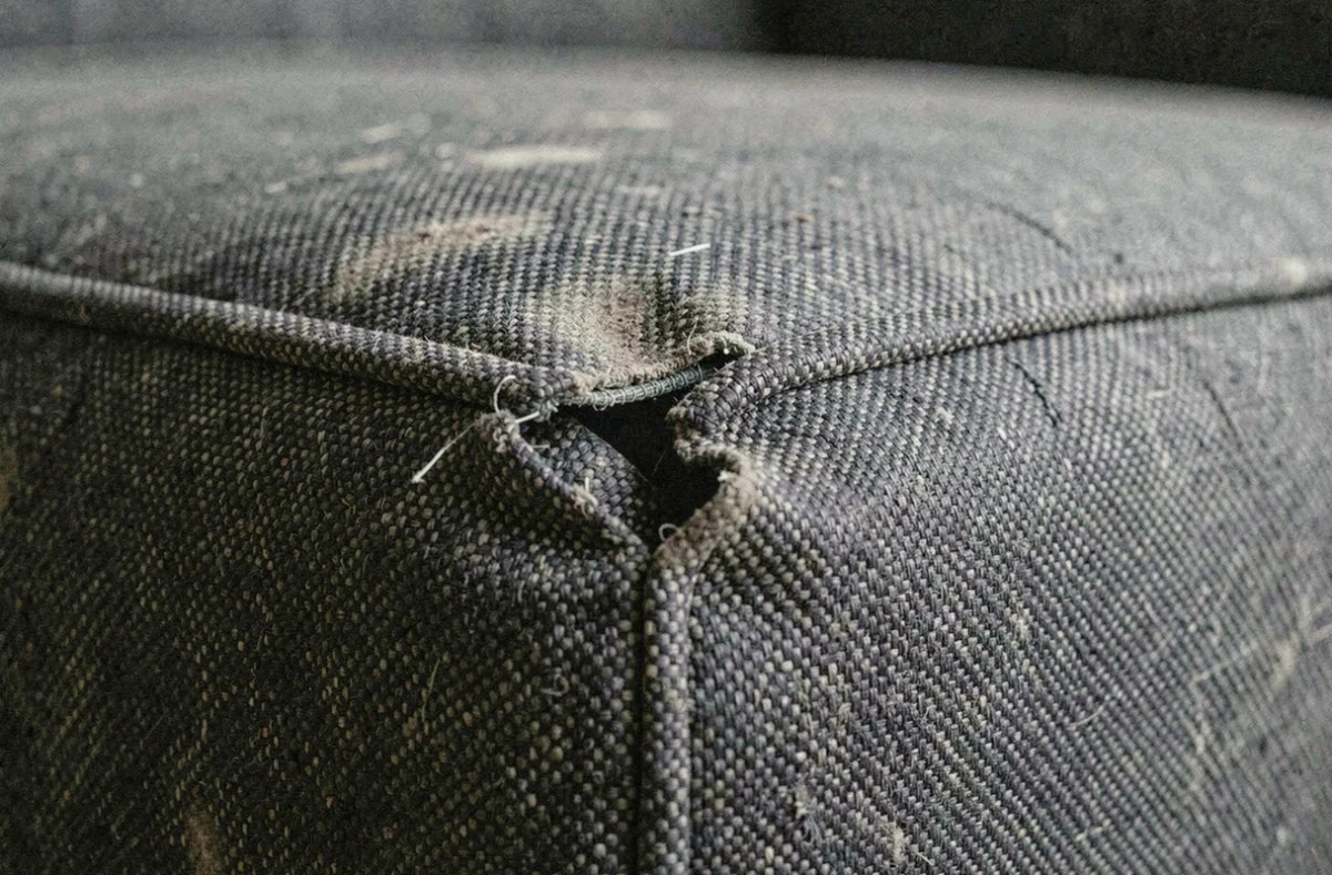 Couture de canapé qui se découd avec fil lâche et tissu usé visible en gros plan