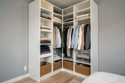 Dressing fonctionnel en panneaux blancs modulables de type Brico Dépôt, avec penderie, étagères et rangements en osier dans une chambre moderne